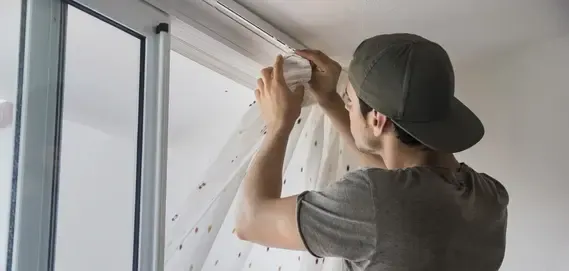 A man in a cap hangs sheer curtain